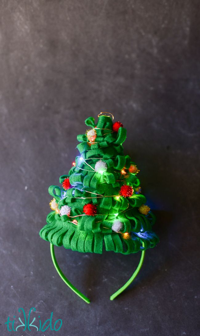 a small green christmas tree with lights on it's headband, sitting on a table