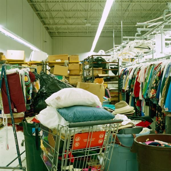 a shopping cart filled with clothes and other items in a room full of hanging racks