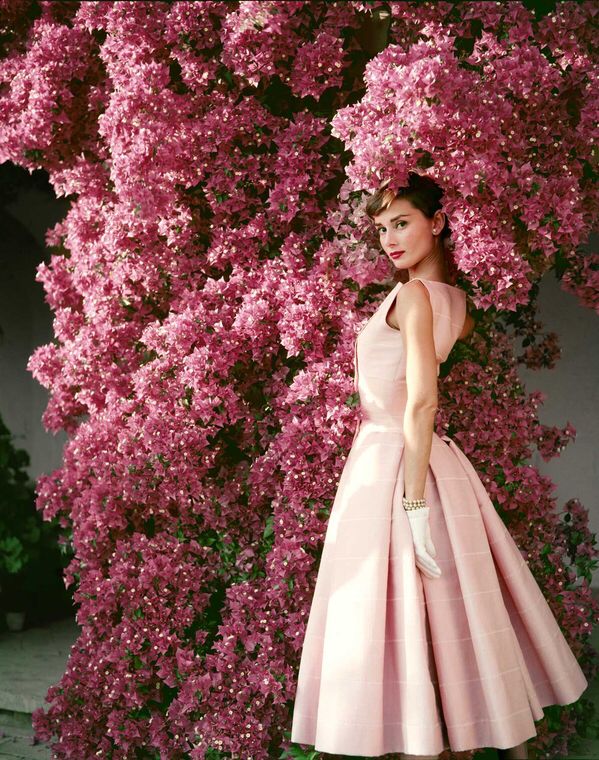 a woman is standing in front of red flowers wearing a long white dress and posing for the camera