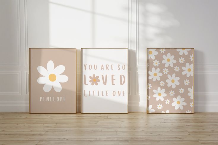 three canvases with flowers on them sitting in front of a wall, one has the words you are so loved and the other is little one