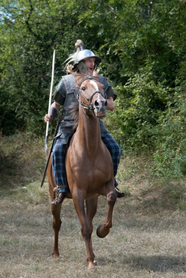 a man riding on the back of a brown horse in a field next to trees