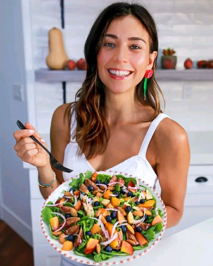 a woman holding a plate of salad in her hands