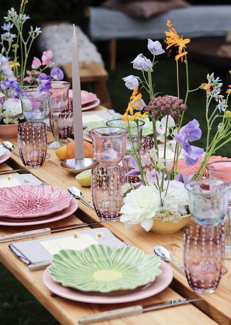 the table is set with pink and green plates, flowers, candles, and napkins