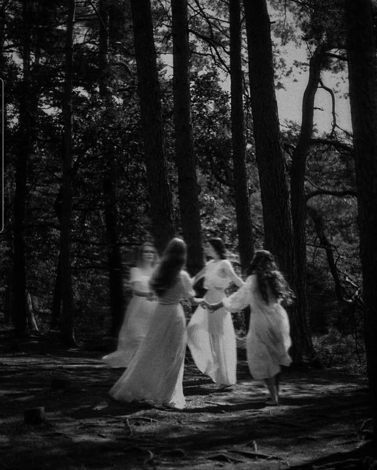 black and white photograph of three women walking through the woods with trees in the background