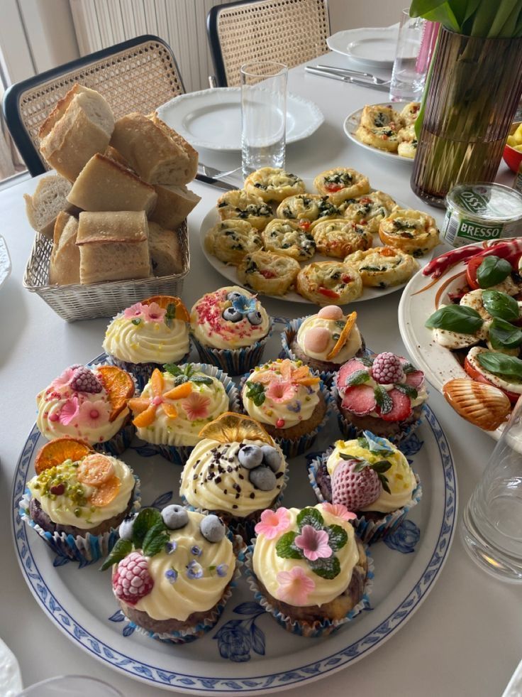 there are many cupcakes on the table with flowers in vases and plates