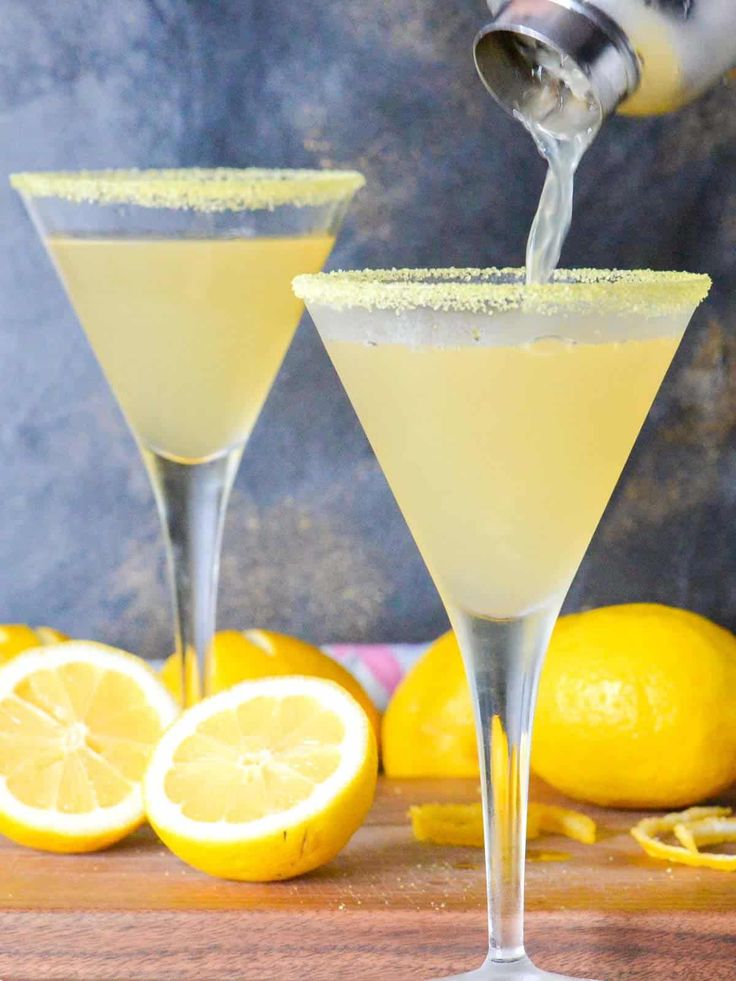 two glasses filled with lemonade sitting on top of a cutting board next to sliced lemons