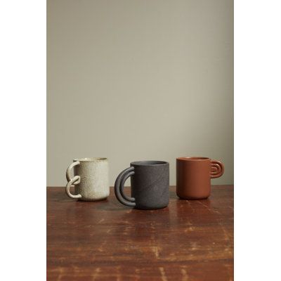 three different colored mugs sitting on top of a wooden table next to each other