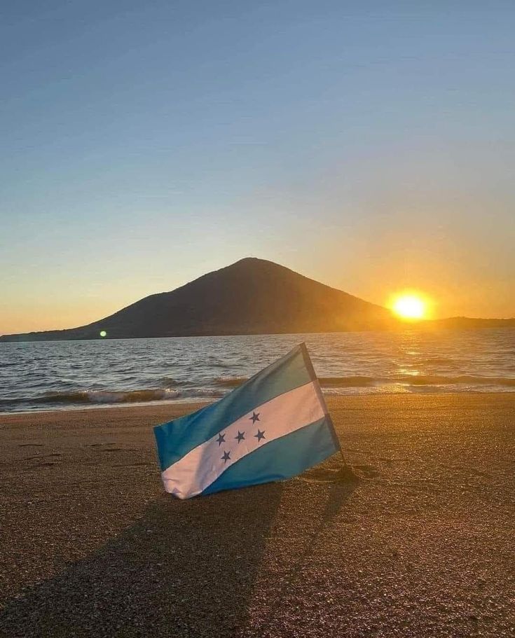 a flag laying on top of a sandy beach next to the ocean with a mountain in the background