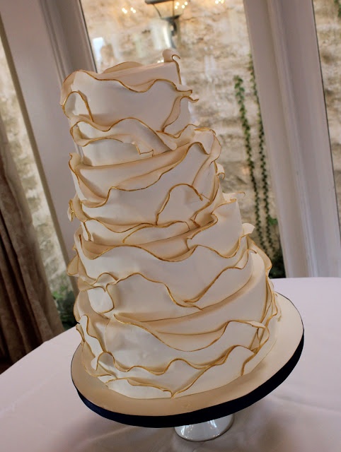 a white and gold wedding cake sitting on top of a table next to a window