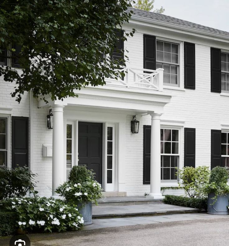 a large white house with black shutters on the front door and windows, along with potted plants