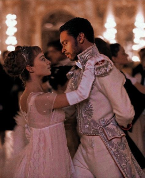 a man and woman dressed in white dance together at a formal event with lights on the walls behind them