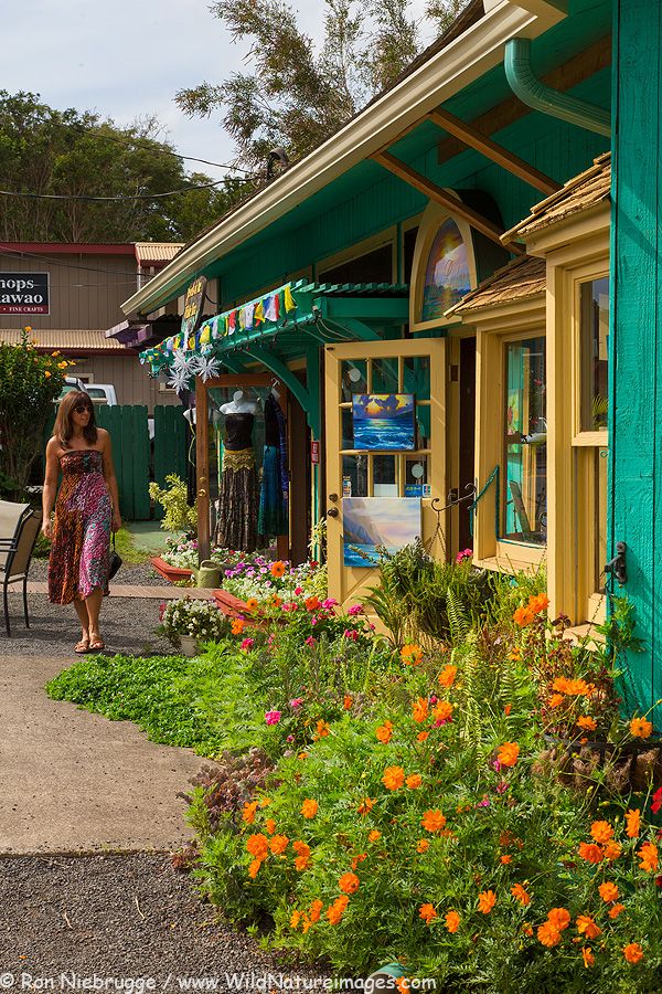 a woman walking down a sidewalk next to a green building with orange flowers in the foreground