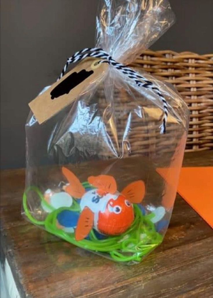 a plastic bag with an orange and blue fish in it sitting on top of a wooden table