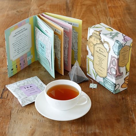 a cup of tea next to an open book on a wooden table with other books