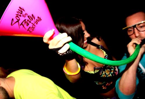 a man holding a pink and green blow dryer in front of his face while two women look on