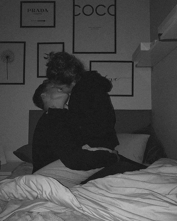 black and white photograph of two people sitting on a bed, one kissing the other