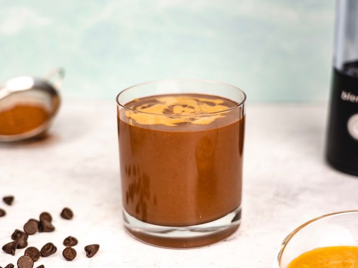 a glass filled with liquid next to some chocolate chips