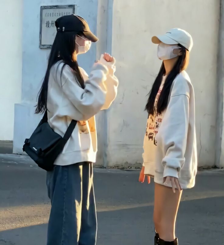 two young women standing on the street with their backs to each other and one is wearing a face mask