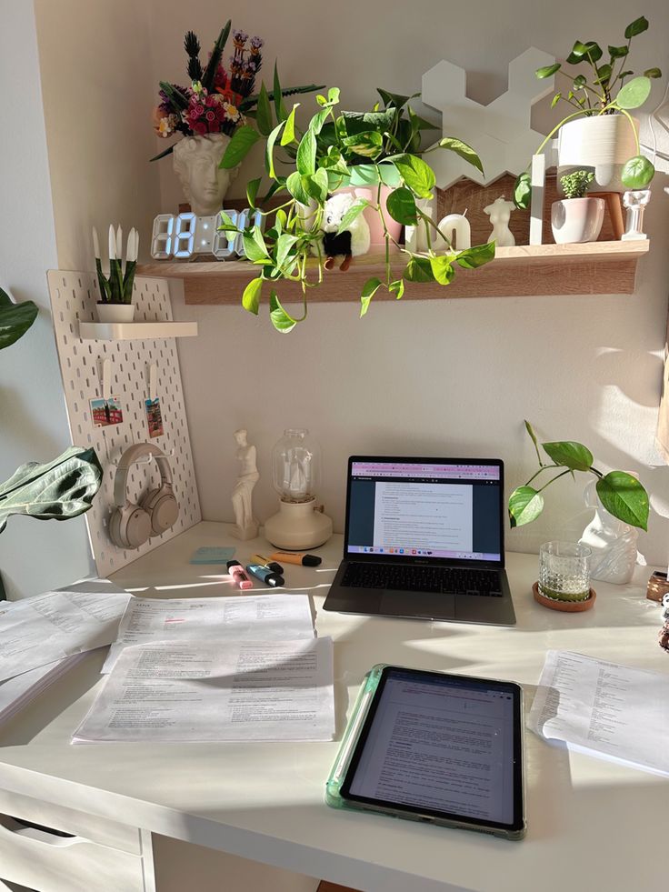 an open laptop computer sitting on top of a white desk next to a potted plant