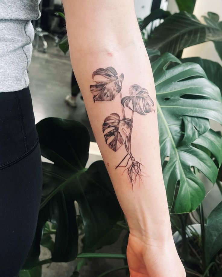 a woman with a tattoo on her arm holding onto a green plant and some leaves