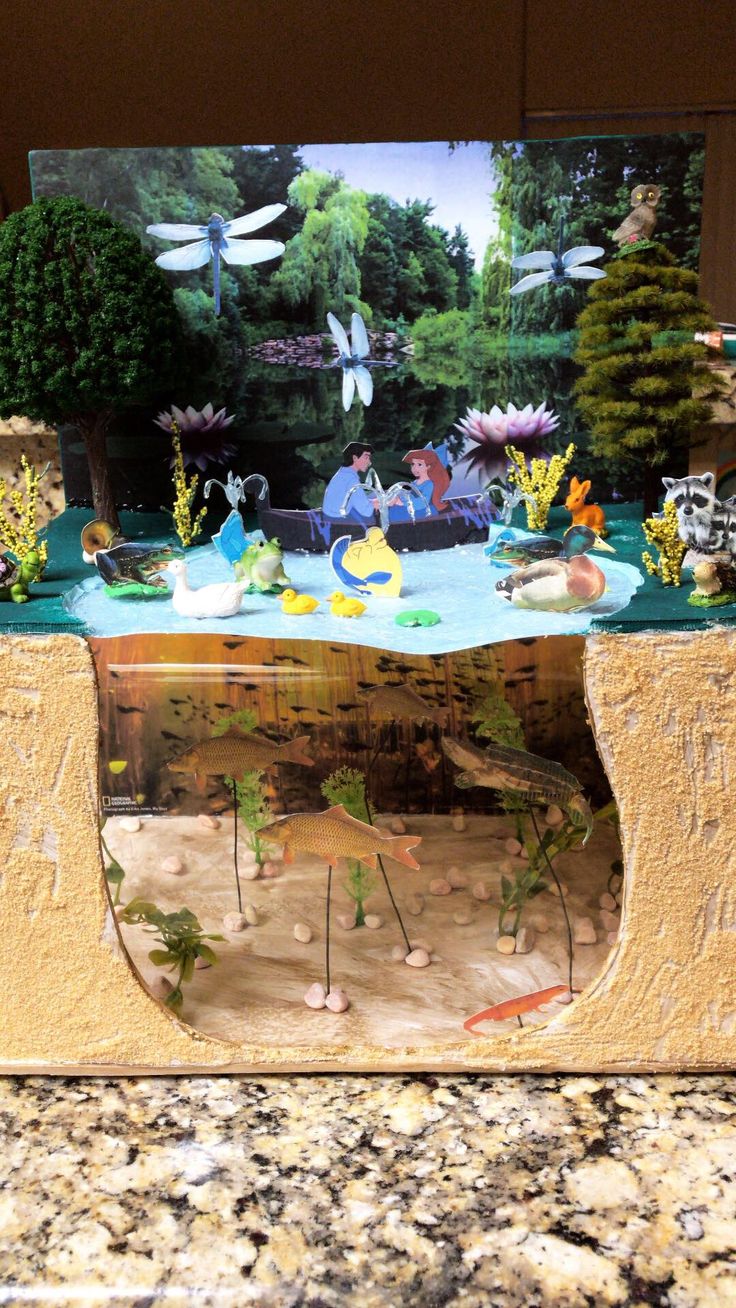 a fish tank with plants and animals in it sitting on a counter top next to a painting