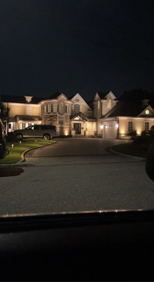 a car parked in front of a large house at night with lights on the windows