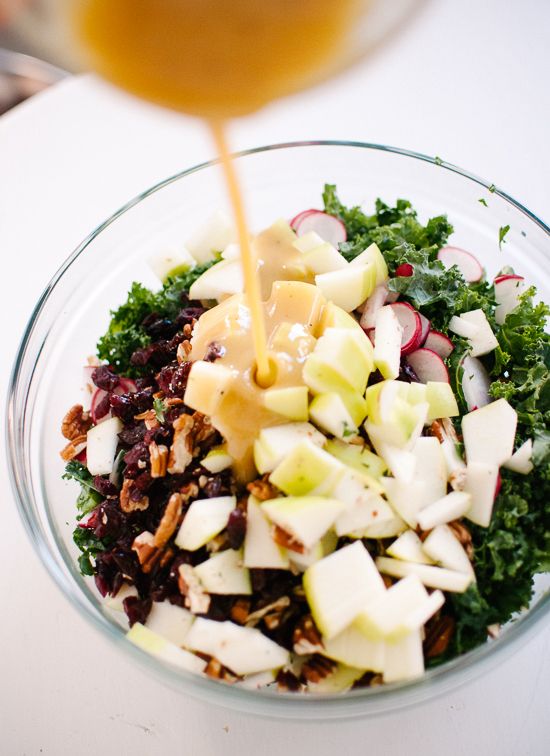 someone pouring dressing into a glass bowl filled with food