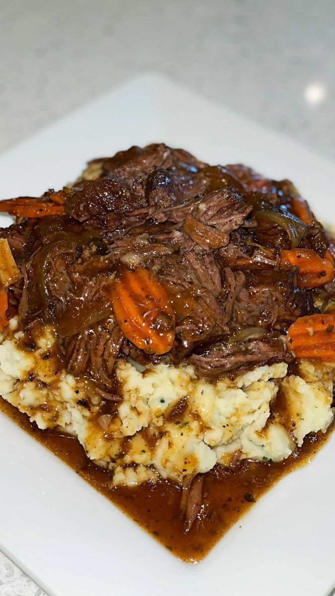 a white plate topped with meat and gravy on top of mashed potatoes