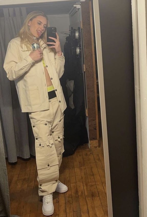 a woman taking a selfie in front of a mirror while wearing white clothing and sneakers