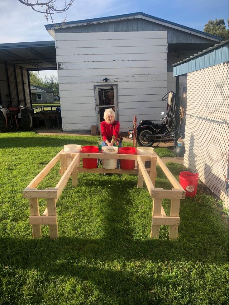 an older woman sitting at a picnic table made out of wooden planks in the grass