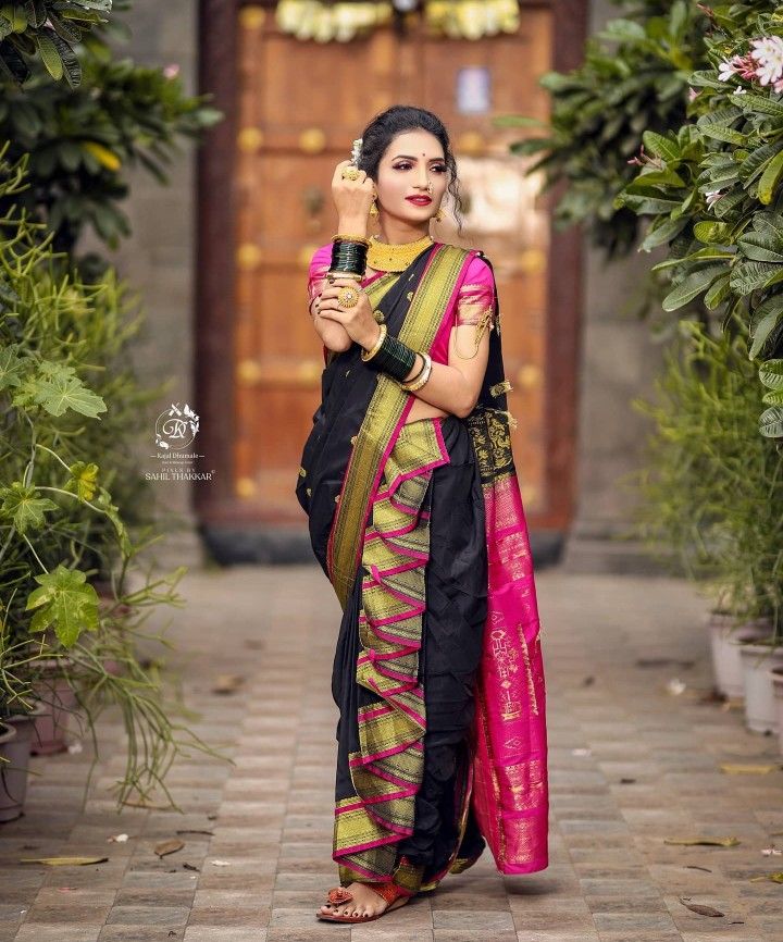 a woman in a black and pink sari standing on a brick walkway with her arms crossed