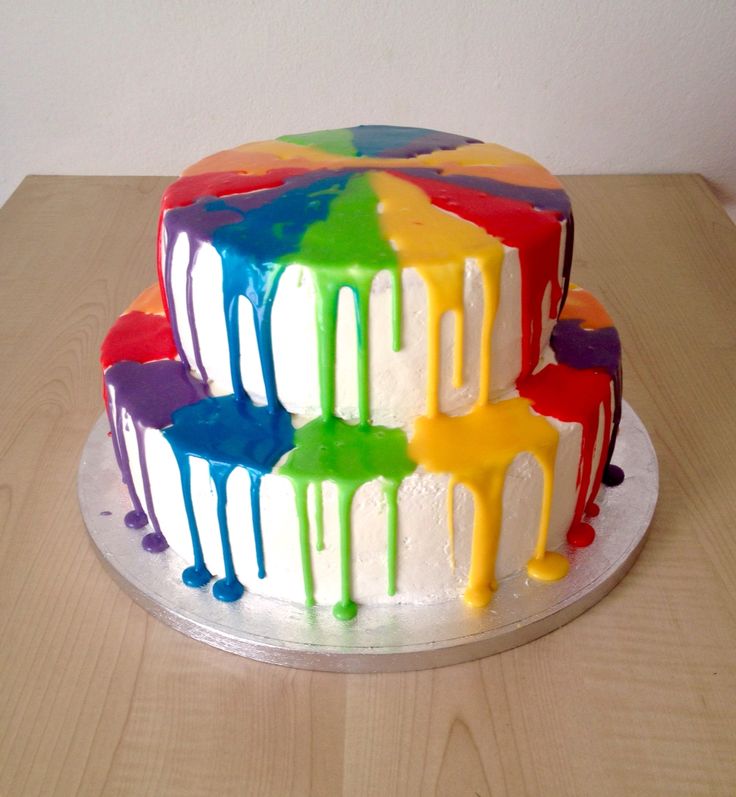 a multicolored cake sitting on top of a wooden table covered in icing