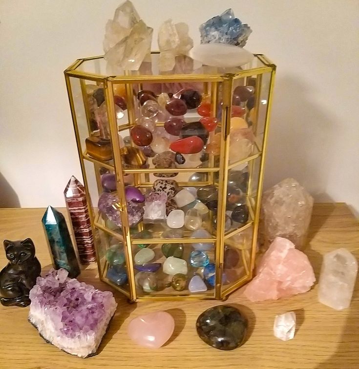 various crystals and rocks sitting on a wooden table next to a gold cage with glass doors