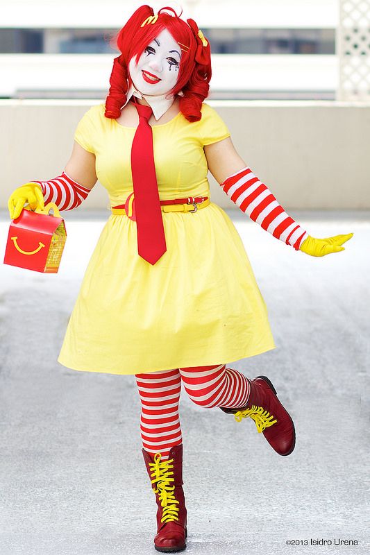 a woman dressed as a clown with red hair and yellow dress, holding a bag