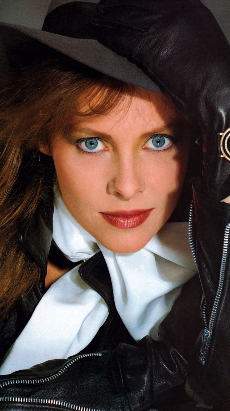 a woman with blue eyes wearing a black hat and leather jacket is posing for the camera