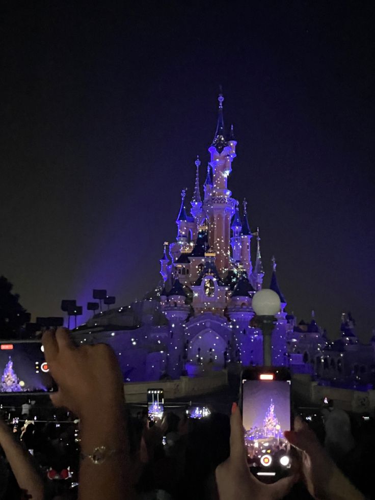 people taking pictures with their cell phones in front of the castle at night, disney world