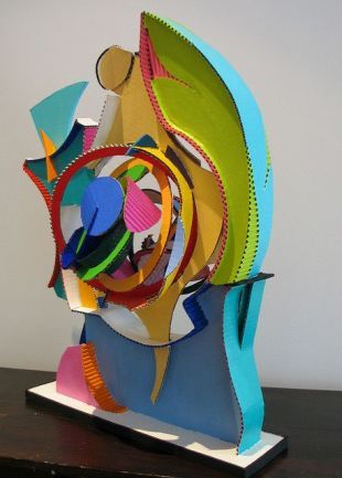 an abstract sculpture made out of paper on top of a wooden table next to a white wall