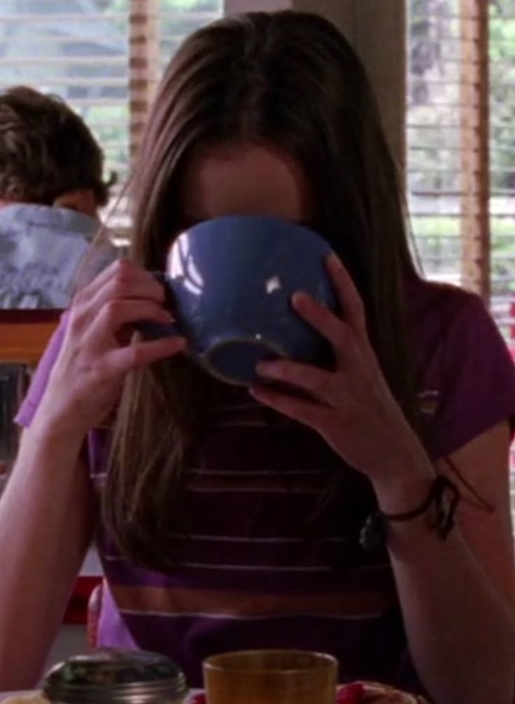 a woman sitting at a table with a bowl in front of her face and looking down