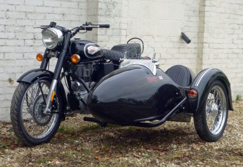 a black motorcycle with sidecar parked next to a brick wall