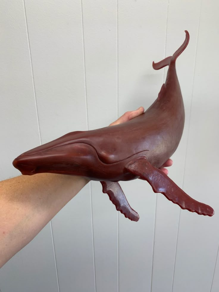 a hand holding a chocolate whale toy in it's right arm, with the tail sticking out