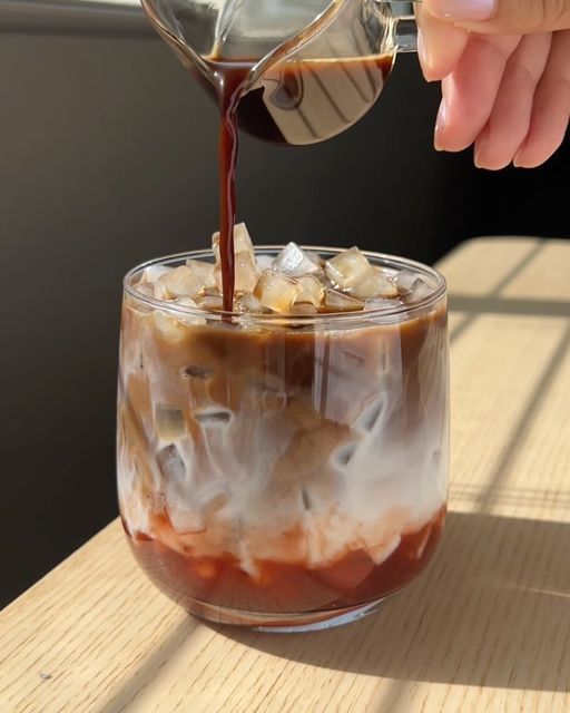 someone pouring coffee into a glass with ice