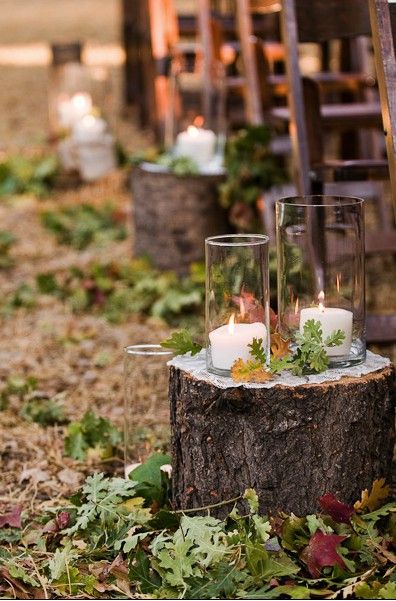 an outdoor ceremony with candles and greenery in glass vases on a tree stump