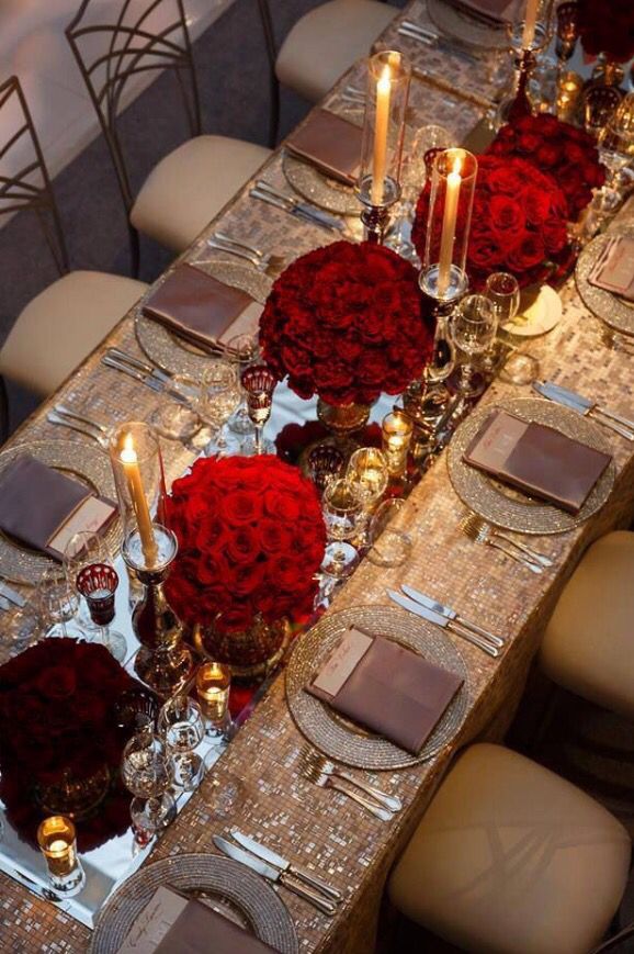 the table is set with red roses and silver place settings for an elegant dinner party