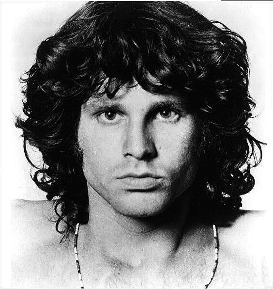 a black and white photo of a man with long curly hair wearing a beaded necklace