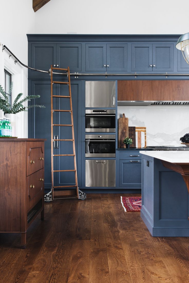 a kitchen with wooden floors and blue cabinets, an oven, ladder to the ceiling