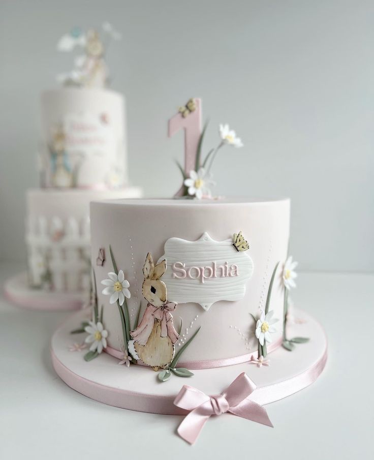 two cakes decorated with pink and white frosting, one has a rabbit on it