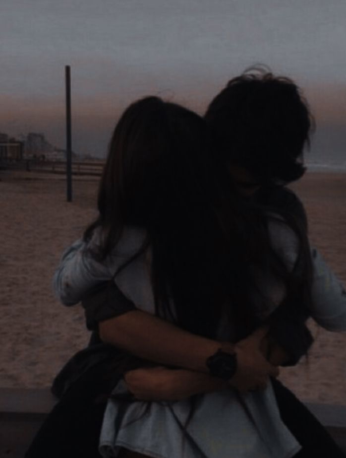 two people hugging each other on the beach at dusk with an overcast sky in the background