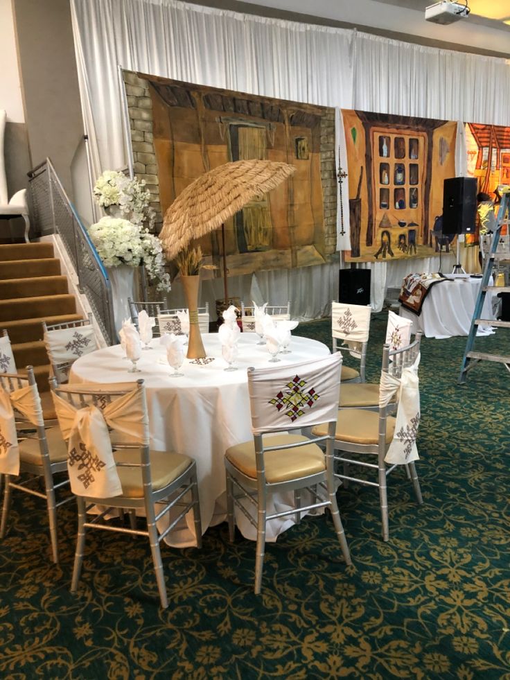 a room filled with tables and chairs covered in white tablecloths under an umbrella