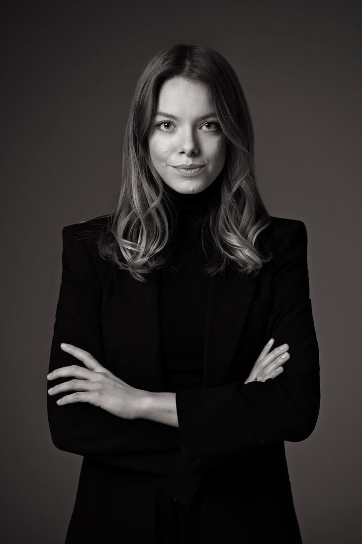 a black and white photo of a woman in a suit with her arms crossed, looking at the camera