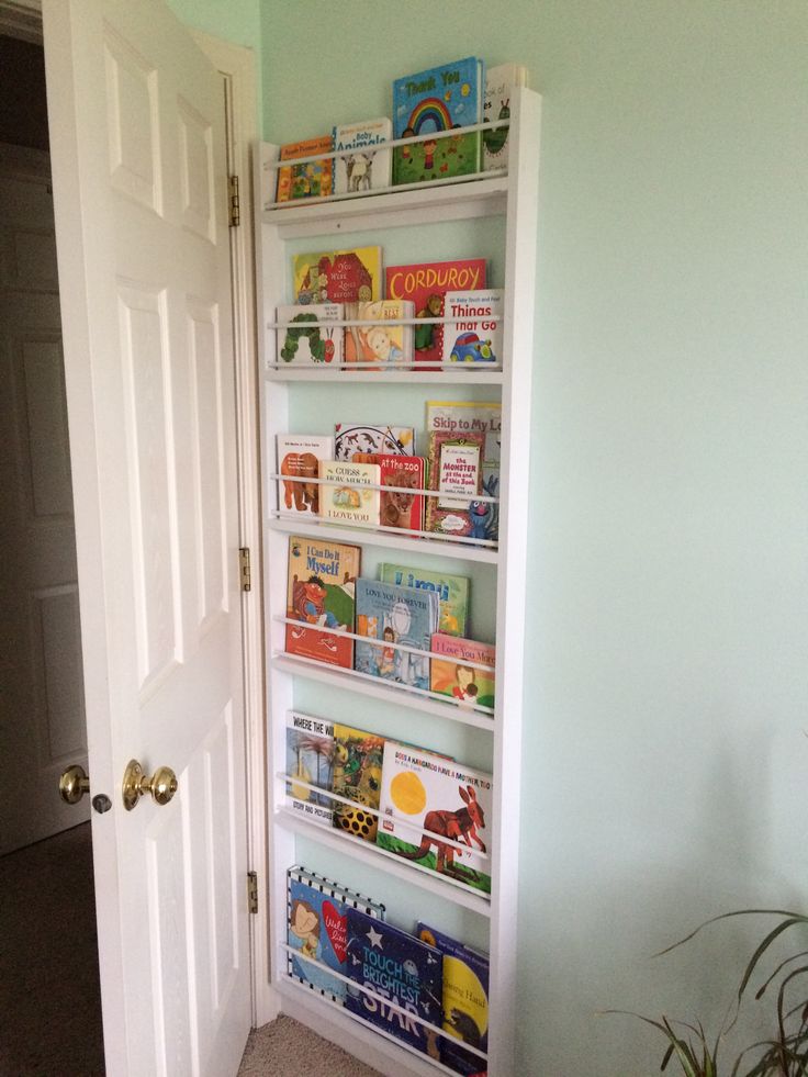 a white book shelf filled with books next to an open door and potted plant